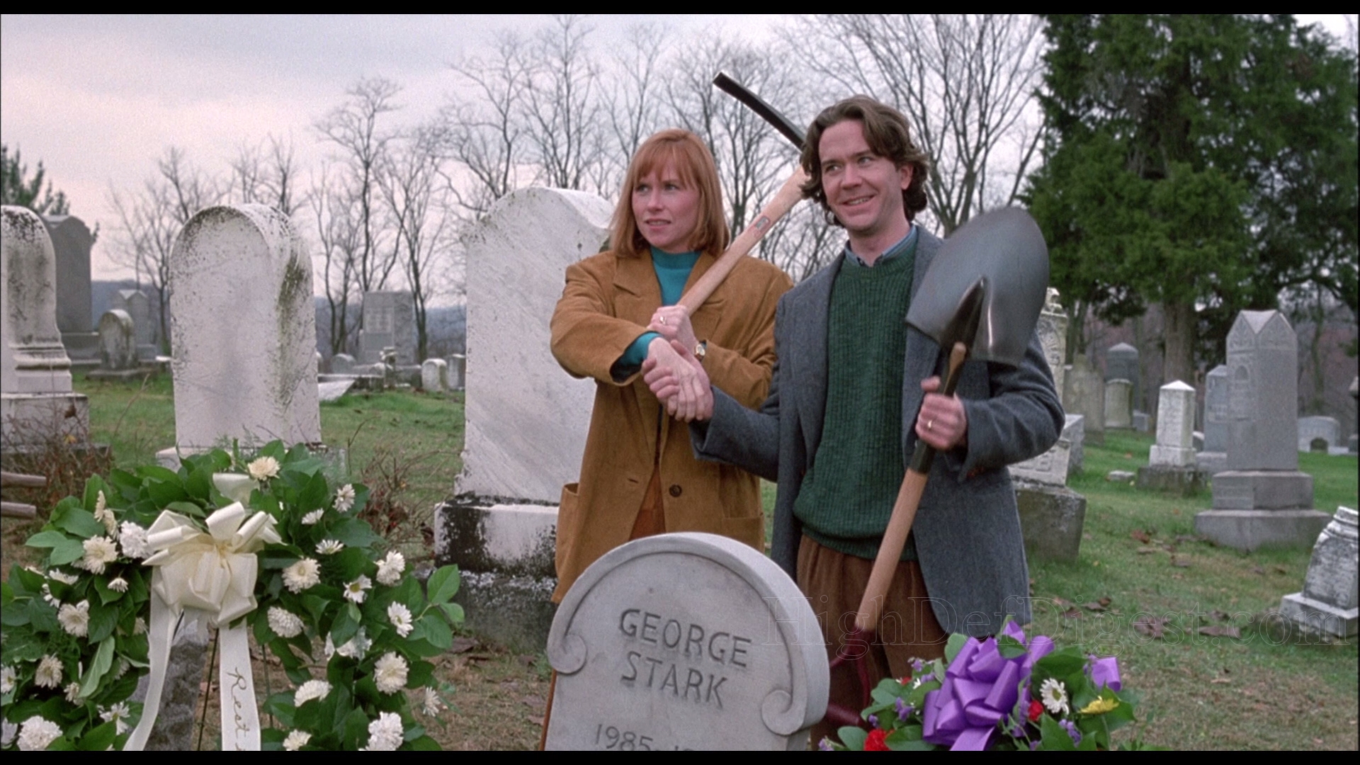 Graveyard scene with woman holding pickax and man holding shovel standing over headstone enscribed George Stark