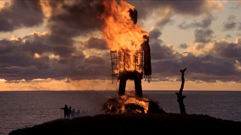 wooden effigy burning with sea in the background at sunset